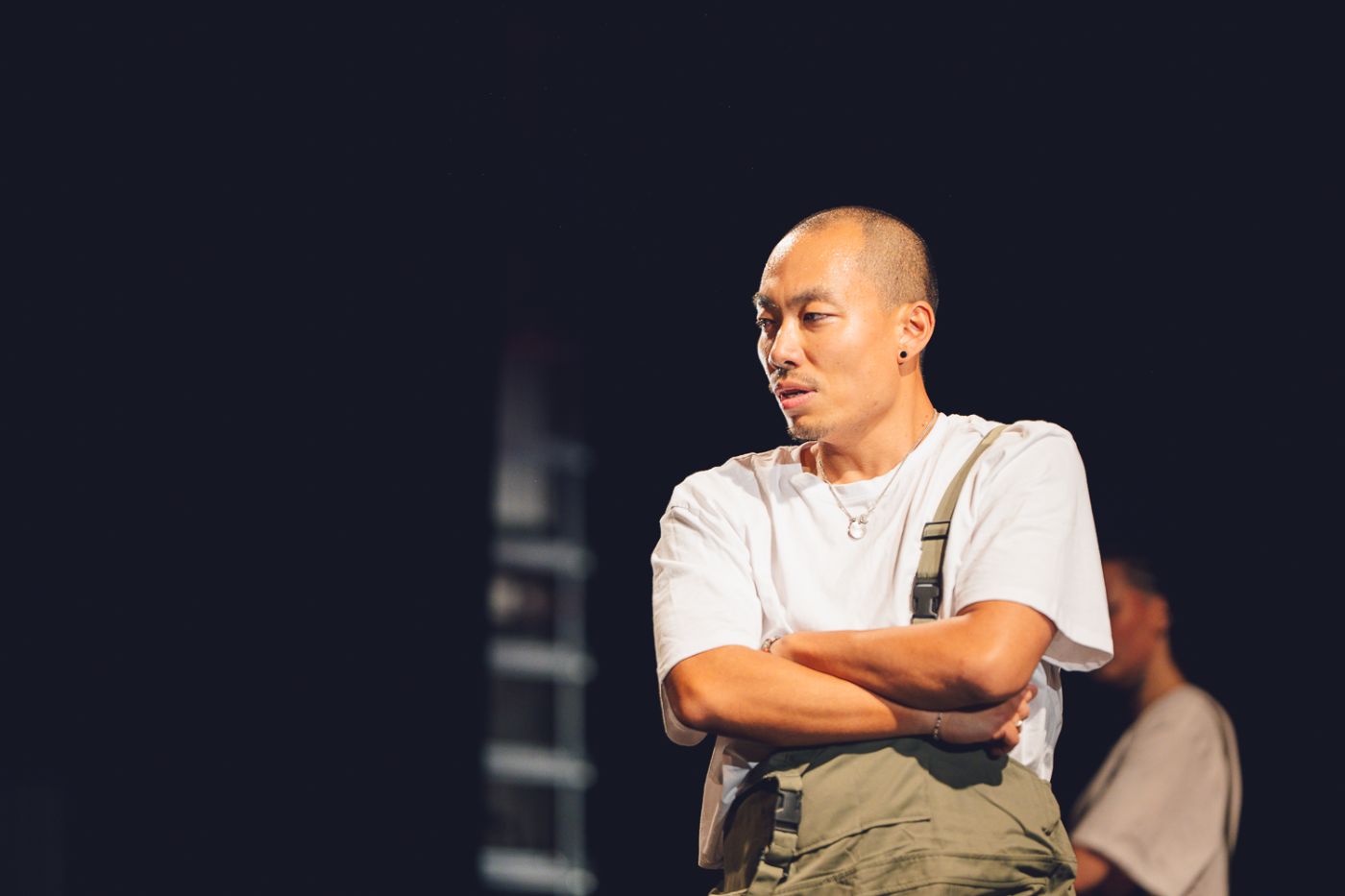 Yi sur scène, bras croisés, le regard tourné vers ses danseurs.